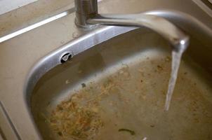 tapón del fregadero de acero inoxidable cerca del orificio lleno de agua y partículas de comida foto