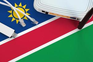 Namibia flag depicted on table with internet rj45 cable, wireless usb wifi adapter and router. Internet connection concept photo