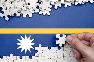 Nauru flag is depicted on a table on which the human hand folds a puzzle of white color photo