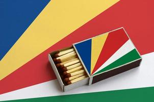 Seychelles flag is shown in an open matchbox, which is filled with matches and lies on a large flag photo