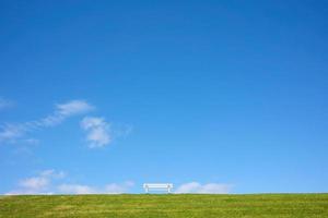 Bench on a green hill, against a background of blue sky and clouds, in a park on a sunny summer day. Beautiful landscape. photo