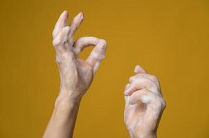 manos en espuma jabonosa, una de ellas muestra un buen signo con los dedos. concepto de una forma eficaz de prevenir la propagación de infecciones. foto