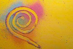 Spiral is drawn on a multicolored, bright powder, on a yellow background. Copy space. Top view. photo