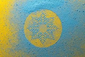 Snowflake, the symbol of winter, is drawn with blue powder on a yellow background. Holiday concept. Top view. photo