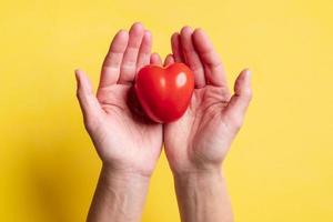 Red tomato in the form of a heart, a symbol of love in the palms, on a yellow background. Healthy food concept. Valentine's Day. photo