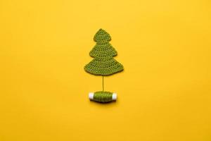 Knitted Christmas tree - a symbol of the New Year, with a spool of thread, on a yellow background. Horizontal photo. photo