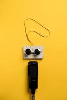 Retro audiotape with magnetic tape in sunglasses and a modern microphone at the bottom. Yellow background. Musical concept. photo