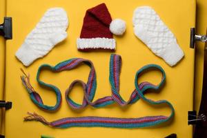 Word SALE is made with a knitted scarf, above it is a Santa Claus hat and mittens. Concept of New Year discounts and shopping. photo