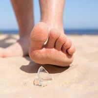Leg walks on the beach and runs the risk of injury, stepping on a shard of broken glass, which is lying on the sandy seashore. photo