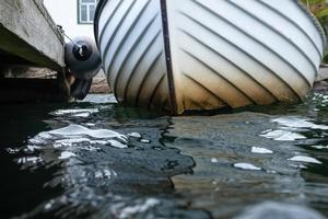 Boat is moored to an old wooden pier with a float, on the seashore. Close-up. photo