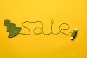 Sale made of green threads going from a knitted Christmas tree to a spool, on a yellow background. Concept of New Years discounts. photo