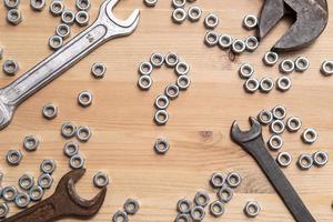 Question mark made of metal nuts on a wooden table, a variety of wrenches lie nearby. Problem solving concept. Top view. photo