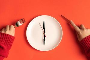 plato con manecillas de hora en forma de tenedor y cuchillo, hora de comer. manos femeninas con tenedor y cuchillo foto