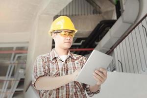 Worker Engineer in Hard Hat Wearing Safety with Touchscreen Tablet Computer. He Works at the Heavy Industry Manufacturing Factory. photo