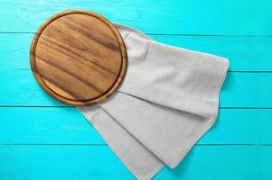 Gray tablecloth and brown cutting board for pizza on blue wooden workplace. Top view and copy space. Mock up photo