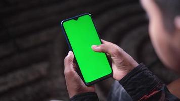 al di sopra di il spalla Visualizza di un' uomo utilizzando un' inteligente Telefono con un' verde schermo video