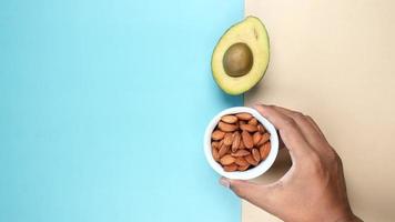 A cup of almonds and half of an avocado, top view video