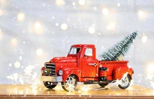 Christmas decor red retro car pickup truck on snow with fairy lights in bokeh Christmas tree. New Year greeting card. Cozy home photo