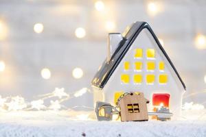 Key to the house with a keychain on a cozy home with a Christmas decor. A gift for New Year, Christmas. Building, design, project, moving to new house, mortgage, rent and purchase real estate photo