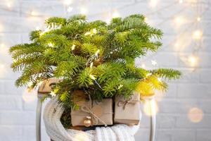 el abeto natural interior en maceta está decorado con bolas como un árbol de navidad con luces de hadas. cajas de regalo con decoración natural para año nuevo y navidad. ecológico, cero residuos, planta doméstica, casa verde. foto