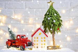 Christmas decor red retro car pickup truck on snow with fairy lights in bokeh Christmas tree. New Year greeting card. Cozy home photo