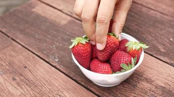 Hand picks a fresh strawberry in a bowl on table video