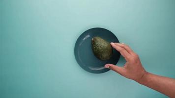 Hand removes whole avocado from plate on blue background video