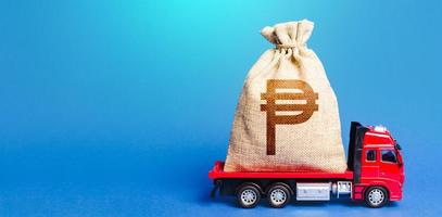 Truck is carrying a big philippine peso money bag. Investment. Anti-crisis measures of government. Attracting large funds to the economy for subsidies, support and cheap soft loans for businesses. photo