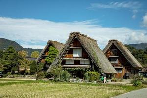 Japanese Shirakawago village during October in autumn fall foliage season. Shirakawa traditional house on triangle roof with a background of rice field, pine mountain and clear cloud sky after. photo