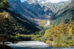 hermoso fondo del centro del parque nacional kamikochi por montañas nevadas, rocas y ríos azusa desde colinas cubiertas de hojas que cambian de color durante la temporada de follaje de otoño. foto