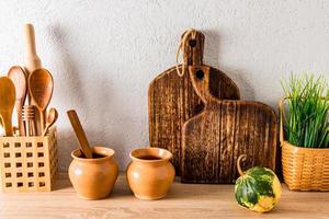 front view of the kitchen countertop of a country house, cottage. homemade kitchen boards, wooden spoons, clay pots. white textured wall. photo