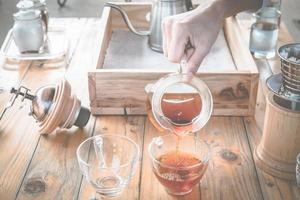 barista sirviendo café de goteo en una taza de vidrio con café de inmersión en el fondo. foto