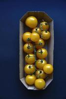 Small cherry tomatoes are yellow and red in a paper container. Small tomatoes on a black background. photo