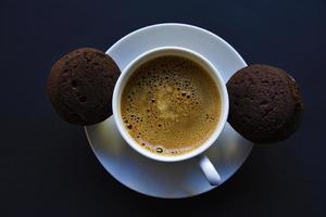 Delicious black coffee with foam in a white cup with sweet cookies. Delicious breakfast with coffee and cookies. Sweet and soft cookies on a black background. photo