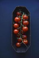 Small cherry tomatoes are yellow and red in a paper container. Small tomatoes on a black background. photo