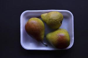 Red and green pears on a black background. Pears in a package from the store. Beautiful fruits of pears. photo