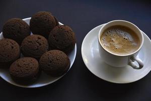 Delicious black coffee with foam in a white cup with sweet cookies. Delicious breakfast with coffee and cookies. Sweet and soft cookies on a black background. photo