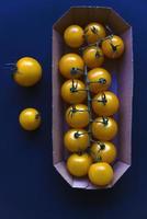 Small cherry tomatoes are yellow and red in a paper container. Small tomatoes on a black background. photo