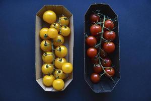 Small cherry tomatoes are yellow and red in a paper container. Small tomatoes on a black background. photo