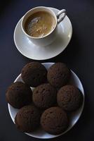Delicious black coffee with foam in a white cup with sweet cookies. Delicious breakfast with coffee and cookies. Sweet and soft cookies on a black background. photo