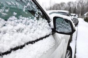 Right side of the car, door and SUV side mirror covered in snow and ice in winter. Negative consequence after heavy snowfall in winter time. Close up, selective focus. Snow-covered urban street view. photo