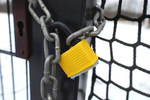 The entrance to sports field is closed with a massive metal chain and yellow padlock. No access during the winter season to outdoors field. Mesh fencing and lattice gate. Safety and security concept. photo