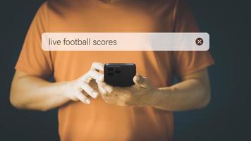 Football fan checking mobile phone gor live football scores in his home. Searching Browsing Internet Data Information with search bar. Search Engine technology networking Concept. photo