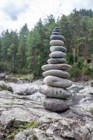 A pyramid of bare stones stacked on top of each other. Stones stacked in the shape of a pyramid on the riverbank against the background of mountains as balance and balance in nature, Zen, Buddhism. photo