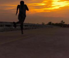 silueta de un hombre corriendo hacia el sol en un puente al atardecer. foto