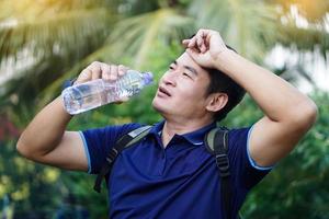 un apuesto viajero asiático sostiene una botella de agua potable para beber al aire libre. concepto, agua potable para la salud, estilo de vida saludable. saciar la sed, reducir la fatiga, refrescar el cuerpo. foto