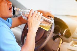 un borracho asiático sostiene una botella de brandy para beber en el auto. concepto, deja de conducir mientras bebes alcohol o campaña de whisky. ilegal y peligroso conducir un vehículo que conduce a un accidente. foto