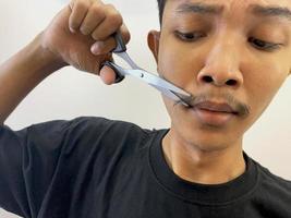 man cutting his own beard using scissors by himself photo