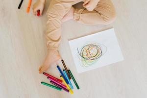 primer plano de la mano de un niño sentado en casa en el suelo y dibujando un dibujo con lápices de colores. desarrollo infantil foto