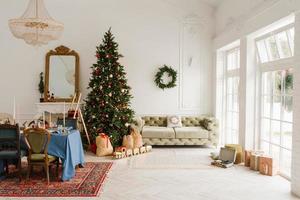 el clásico interior navideño de año nuevo de la habitación está decorado con un árbol de navidad. árbol de navidad con adornos dorados y rojos y cajas de regalo. nochebuena en casa foto